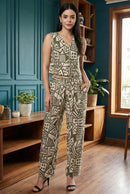Woman wearing a patterned jumpsuit standing in a room with wooden furniture and plants.