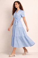Woman wearing a light blue mazi dress against a beige background