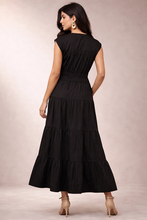 Woman wearing a black tiered dress against a neutral background