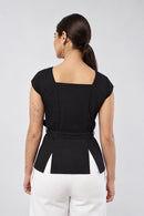 A woman shown from the back wearing a rust-orange peplum top with a square neckline and a matching waist tie, paired with black pants, in an indoor setting.