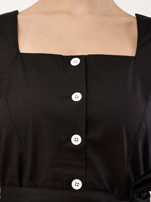 Close-up of a black cotton-like top with a square neckline, front button closure, and white buttons, shown on a model.