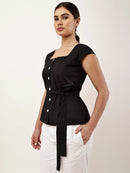 A woman modeling a black peplum-style top with a square neckline, cap sleeves, front buttons, and a self-tie waist belt, paired with white pants against a plain light background.