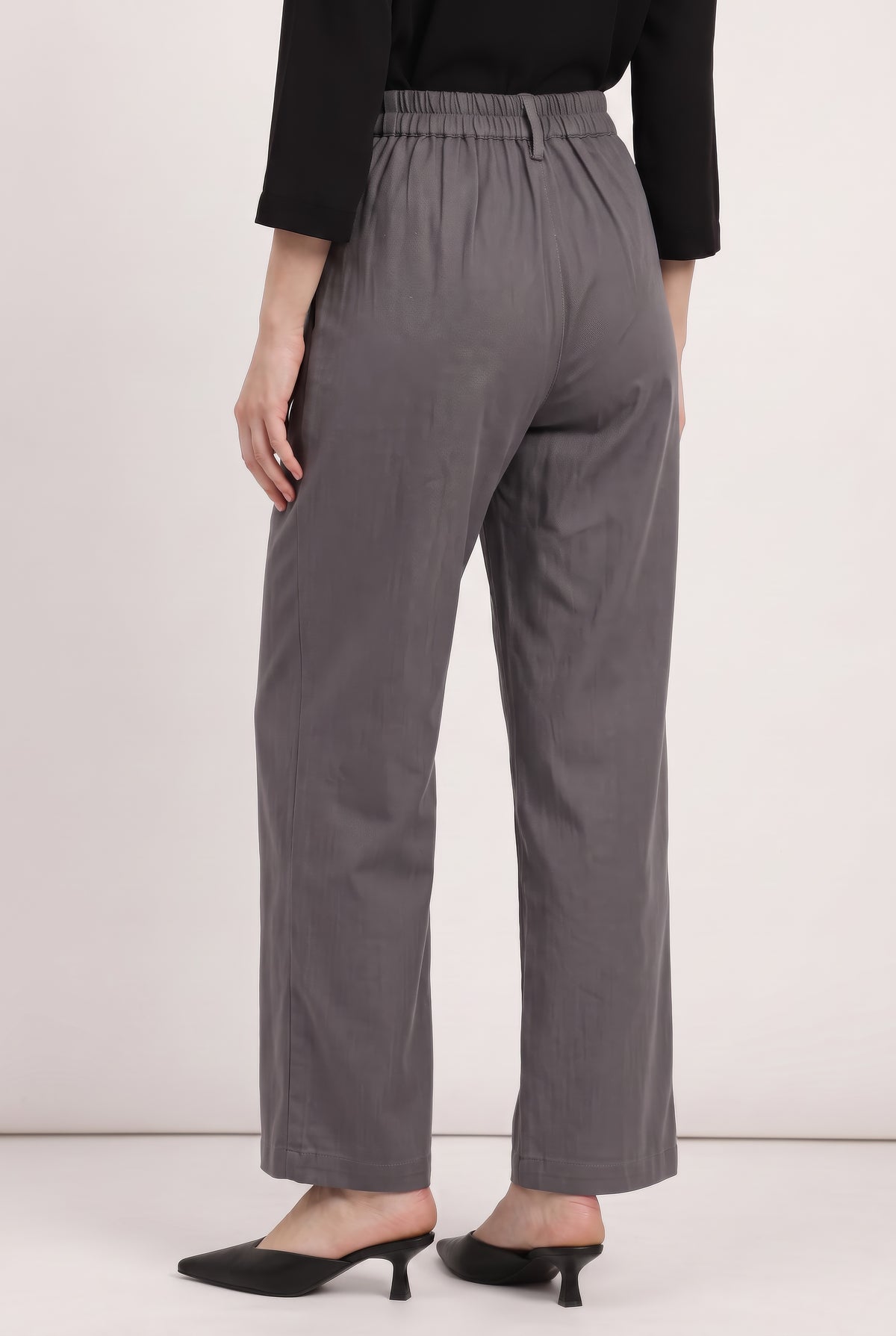 A model from the back wearing gray wide-leg trousers, a black long-sleeve top, and black pointed-toe mule heels against a plain light background.
