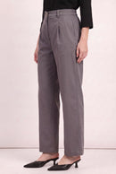 A model wearing high-waisted, wide-leg gray trousers with a front pleat detail, styled with a black top and black pointed-toe mule heels against a light pink studio background.