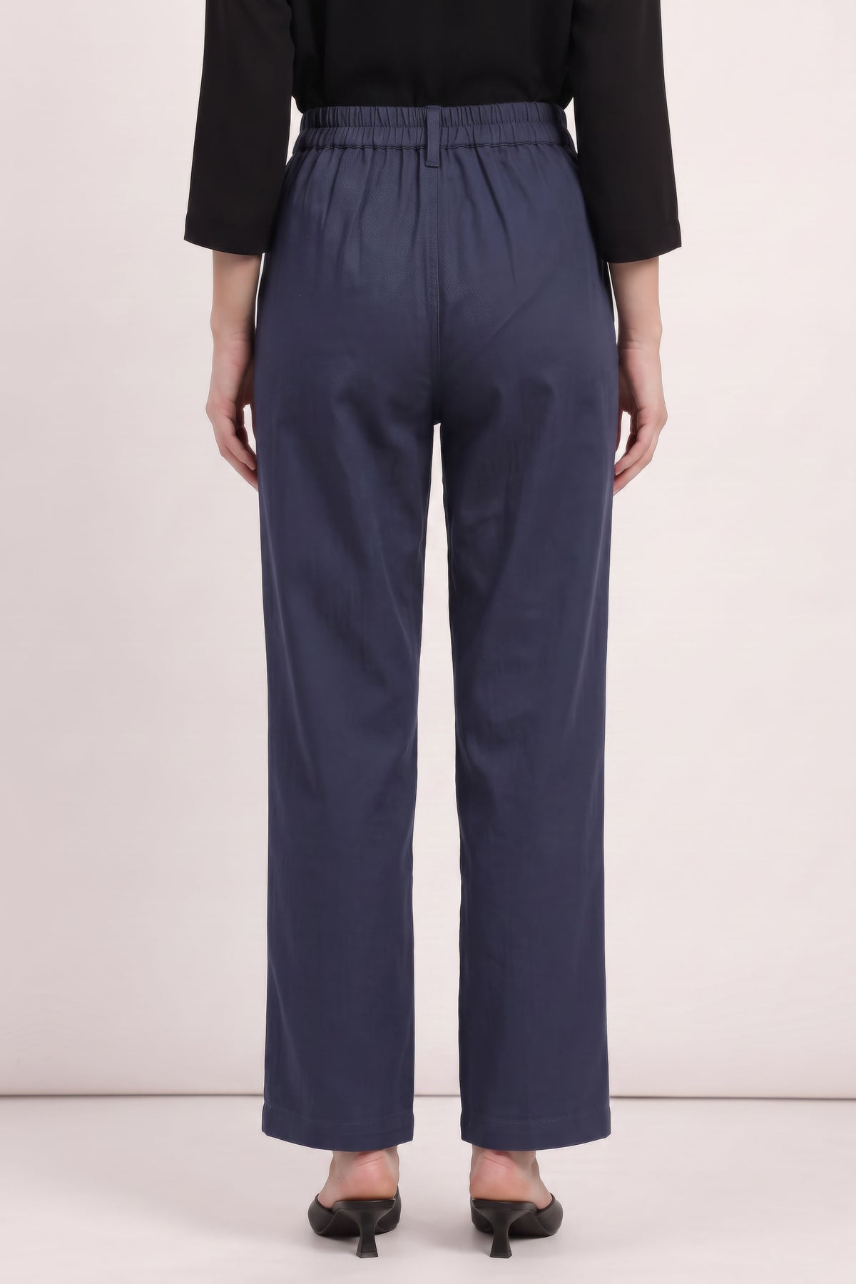 A person shown from the back wearing navy wide-leg cropped pants with an elastic waistband, paired with a black long-sleeve top and black pointed-toe heels, against a plain light beige studio background.