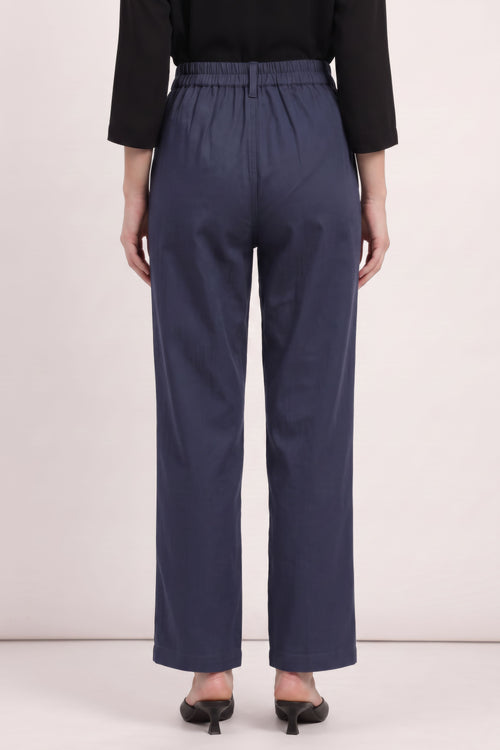 A person shown from the back wearing navy wide-leg cropped pants with an elastic waistband, paired with a black long-sleeve top and black pointed-toe heels, against a plain light beige studio background.