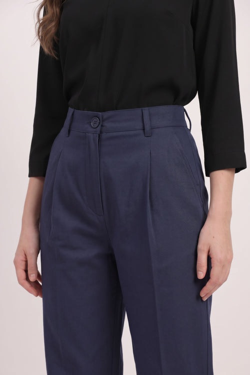 A close-up of a person wearing navy blue high-waisted pleated trousers and a black long-sleeve top, shown from the chest down against a plain light background.