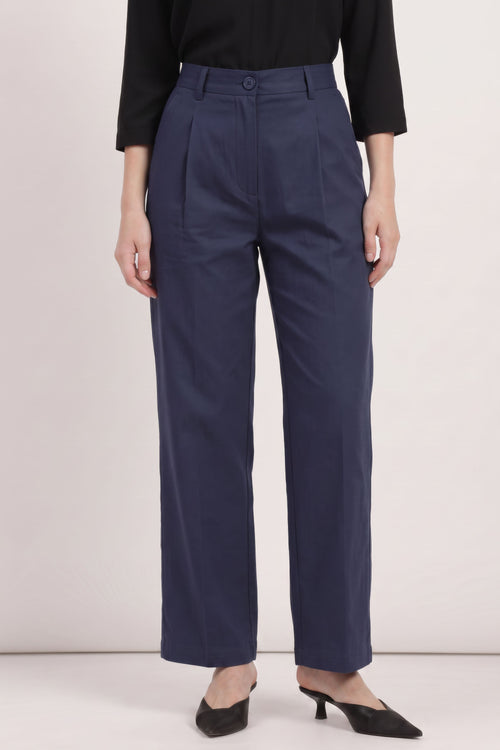 A model wearing navy blue wide-leg trousers with pleated details, paired with a black long-sleeve top and black pointed-toe mule heels, against a plain light background.