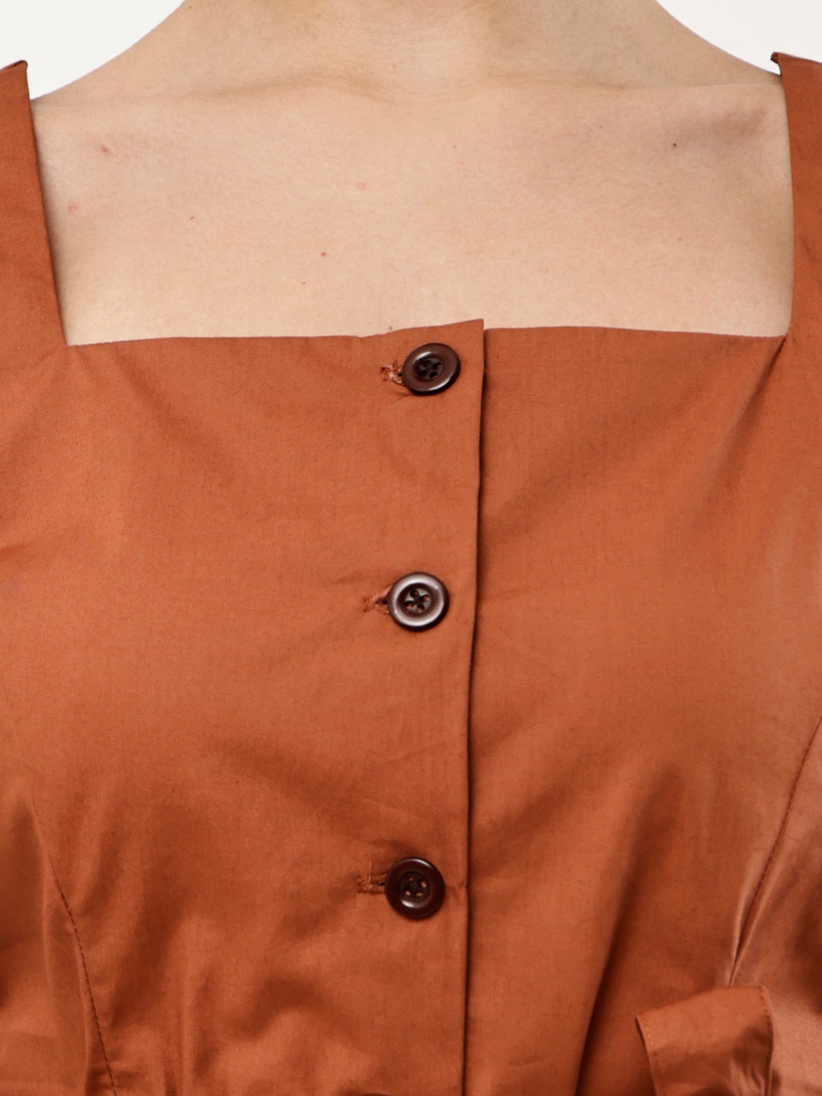 Close-up of a terracotta brown top with a square neckline, three dark brown buttons, and a visible skin line at the neck.