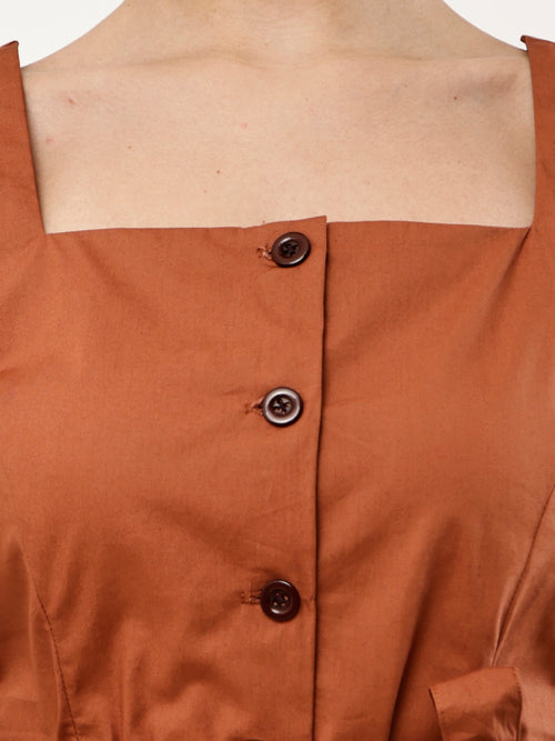 Close-up of a terracotta brown top with a square neckline, three dark brown buttons, and a visible skin line at the neck.