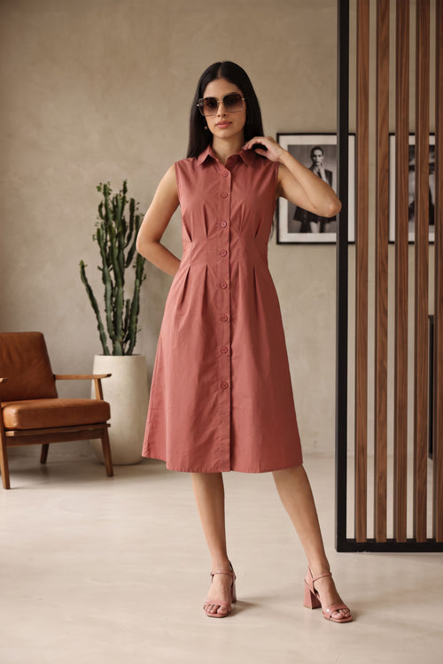 A woman models a sleeveless, button-front midi dress in a dusty rose pink color, styled with sunglasses and pink block-heel sandals in a modern indoor setting.