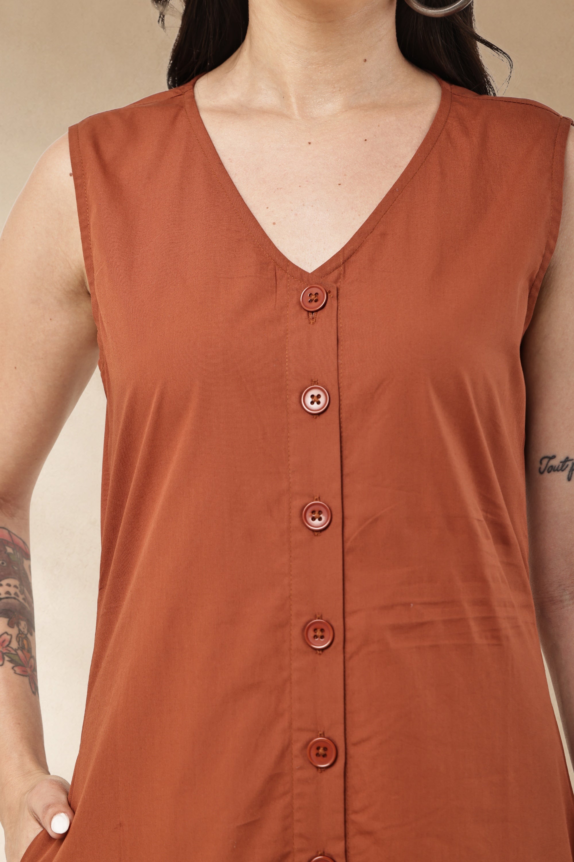 A close-up of a woman wearing a sleeveless rust-orange V-neck top with a button-front placket and matching buttons.