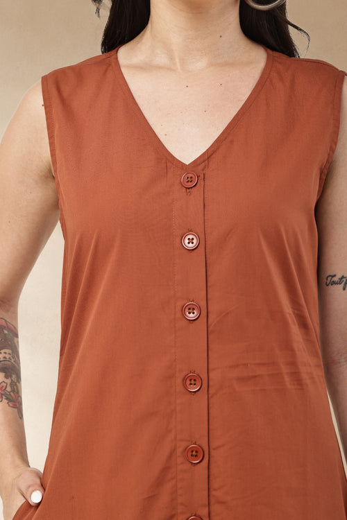 A close-up of a woman wearing a sleeveless rust-orange V-neck top with a button-front placket and matching buttons.