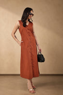 A woman models a sleeveless rust-orange midi dress with a button-down front and side pockets, styled with a black handbag and clear high-heeled sandals against a warm beige studio backdrop.