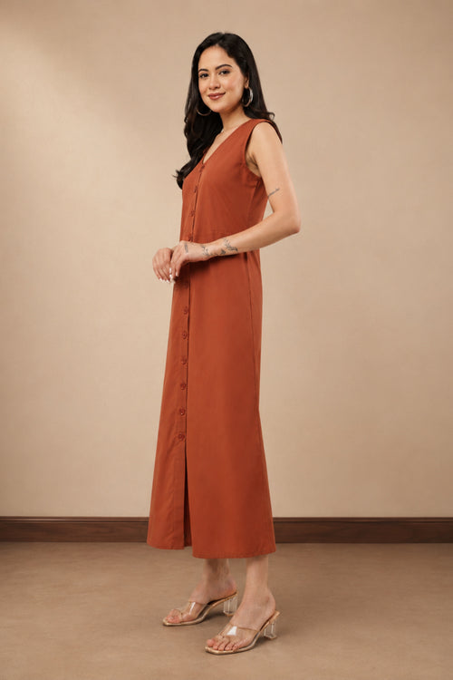 A woman modeling a sleeveless rust-orange maxi dress with a button-front detail, standing against a plain beige studio wall.