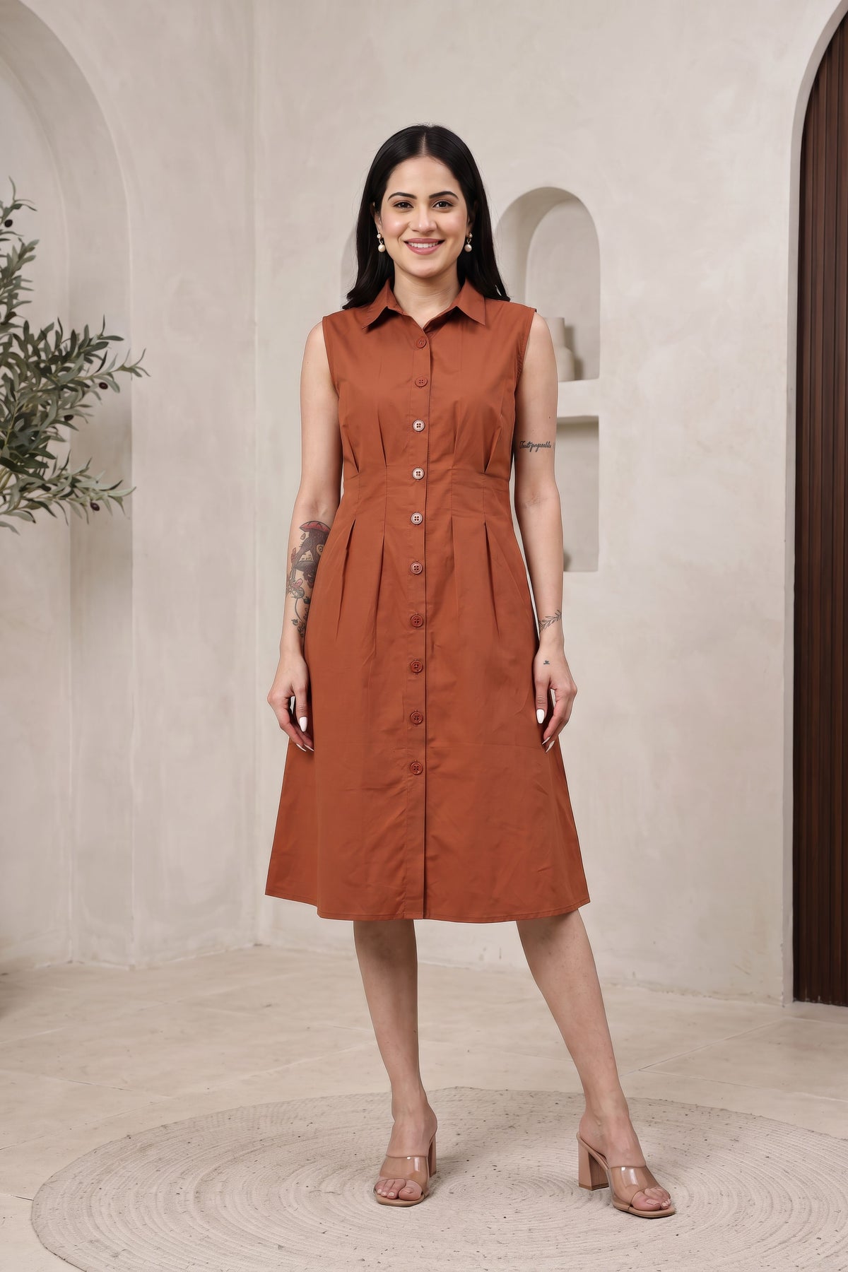 A woman modeling a black sleeveless maxi dress with a spread collar and flared skirt, standing in front of a beige stone archway background.